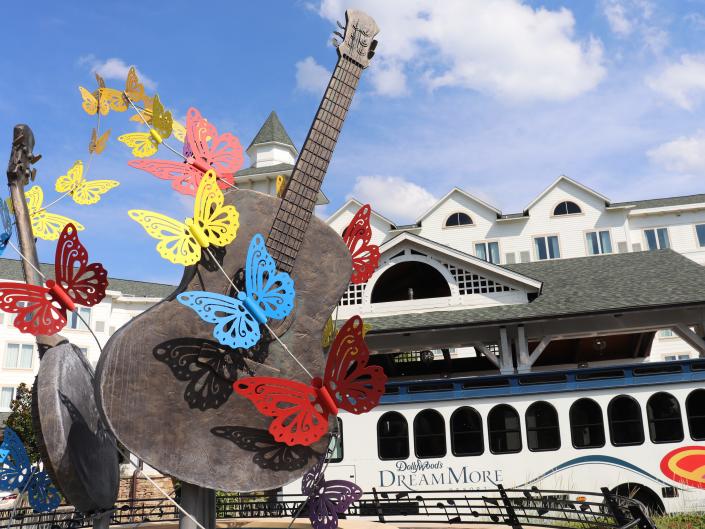 Outside the Dollywood DreamMore Resort. A guitar-shaped statue with butterflies in the foreground, the white hotel building in the background