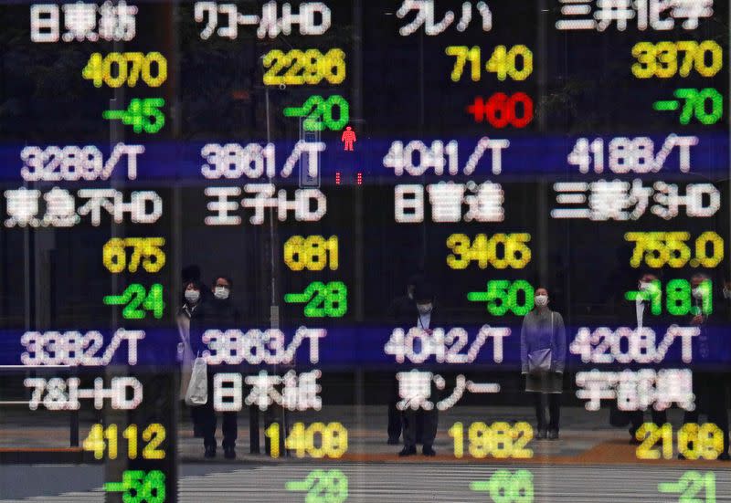 FILE PHOTO: Pedestrians and a traffic light stop sign are reflected on a quotation board in Tokyo