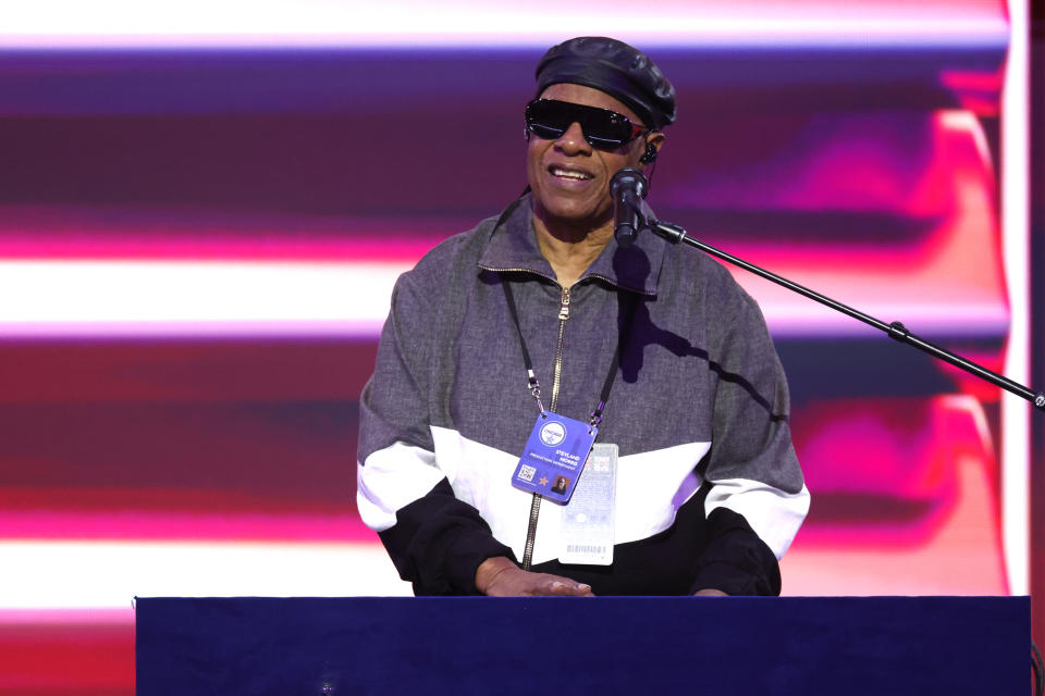 Stevie Wonder trägt eine dunkle Sonnenbrille und einen Hut und tritt mit einem Mikrofon vor ihm auf der Bühne auf