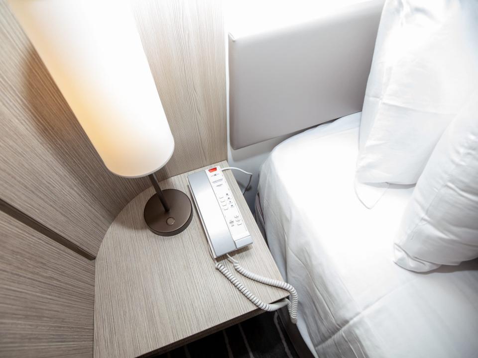 a nightstand with a lamp and phone next to the bed