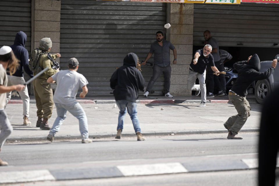 A Palestinian man throws a stone at Israeli settlers and an Israeli soldier during clashes in Huwara, near the West Bank town of Nablus, Thursday, Oct. 13, 2022. (AP Photo/Majdi Mohammed)