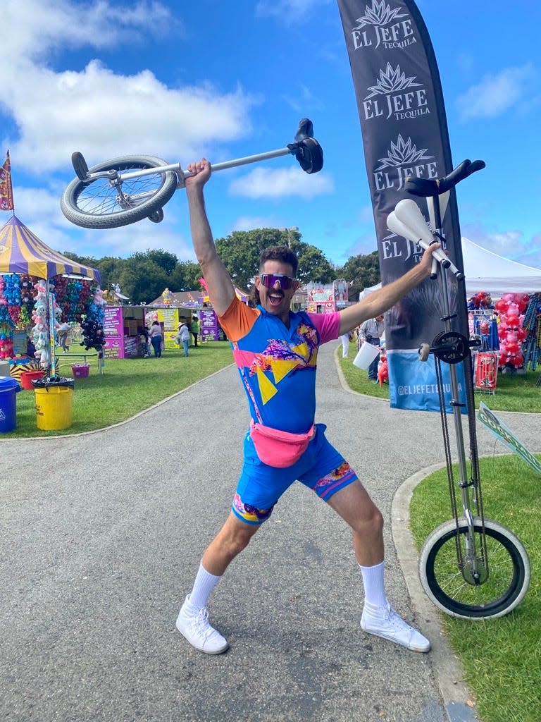 Image description: Mark Wilder in a colorful romper, holding two unicycles and juggling sticks.