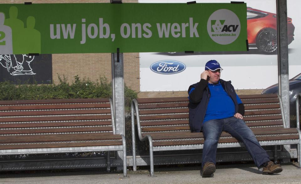 A man sits on a bench and speaks on his cell phone in front of the Ford factory in Genk, Belgium on Wednesday, Oct. 24, 2012. On Wednesday the Ford Motor Co. announced it would close one of its main factories in eastern Belgium by the end of 2014 in a move that will result in 4,500 direct job losses and 5,000 more among subcontractors. Sign reads in Flemish 'Your Job, Our Work'. (AP Photo/Virginia Mayo)