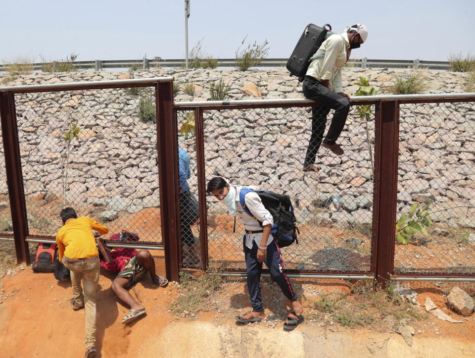 In this Monday, May 4, 2020, photo, migrant workers from the neighboring state of Maharashtra trying to return to their villages hundreds of miles away jump a fence as they walk through a highway during a nationwide lockdown to curb the spread of new coronavirus on the outskirts of Hyderabad, India. Tens of thousands of impoverished migrant workers are on the move across India, walking on highways and railway tracks or riding trucks, buses and crowded trains in blazing heat amid threat to their lives from the coronavirus pandemic. (AP Photo/Mahesh Kumar A.)