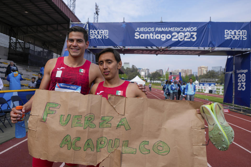 Los mexicanos Emiliano Hernández (derecha) y Duilio Carrillo muestran un cartel de apoyo a Acapulco tras ganar la medalla de oro de los relevos masculinos del pentatlón moderno de los Juegos Panamericanos en Santiago, Chile, el viernes 27 de octubre de 2023. (AP Foto/Matías Delacroix)