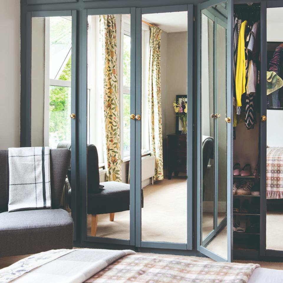 A built-in mirror wardrobe in blue reflecting floral curtains