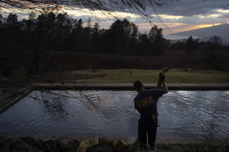 A firefighter pulls a water hose out of a pool after filling it with water for firefighting helicopters in Kula, Hawaii, Tuesday, Aug. 15, 2023. Wildfires have devastated parts of the Hawaiian island of Maui. (AP Photo/Jae C. Hong)