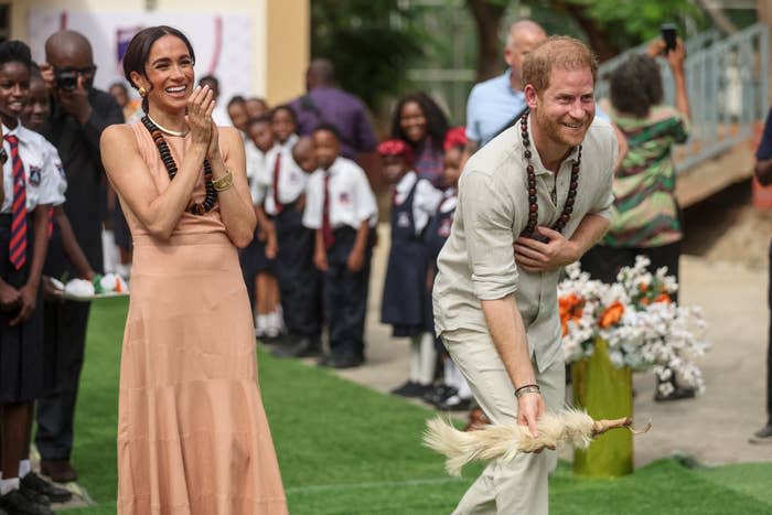 Meghan Markle in a sleeveless dress and Prince Harry playing with children in a casual setting