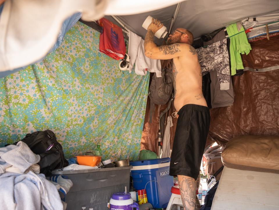 William Nemoff drinks water within his tent in the homeless encampment known as "The Zone" in Phoenix on May 8, 2023.