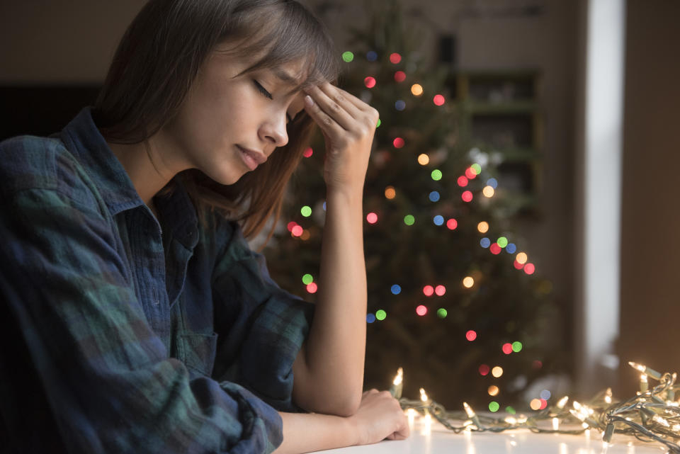 woman is massaging her forehead because of tension and stress while a Christmas tree is in the background