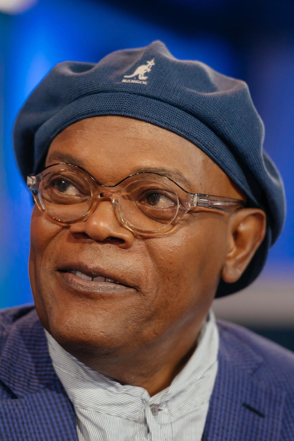 Samuel L. Jackson in a patterned suit and matching cap, seated and looking to the side