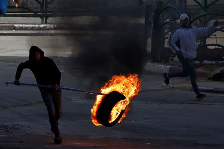 A Palestinian protester moves a burning tire during clashes with Israeli troops in Hebron, in the occupied West Bank March 29, 2019. REUTERS/Mussa Qawasma