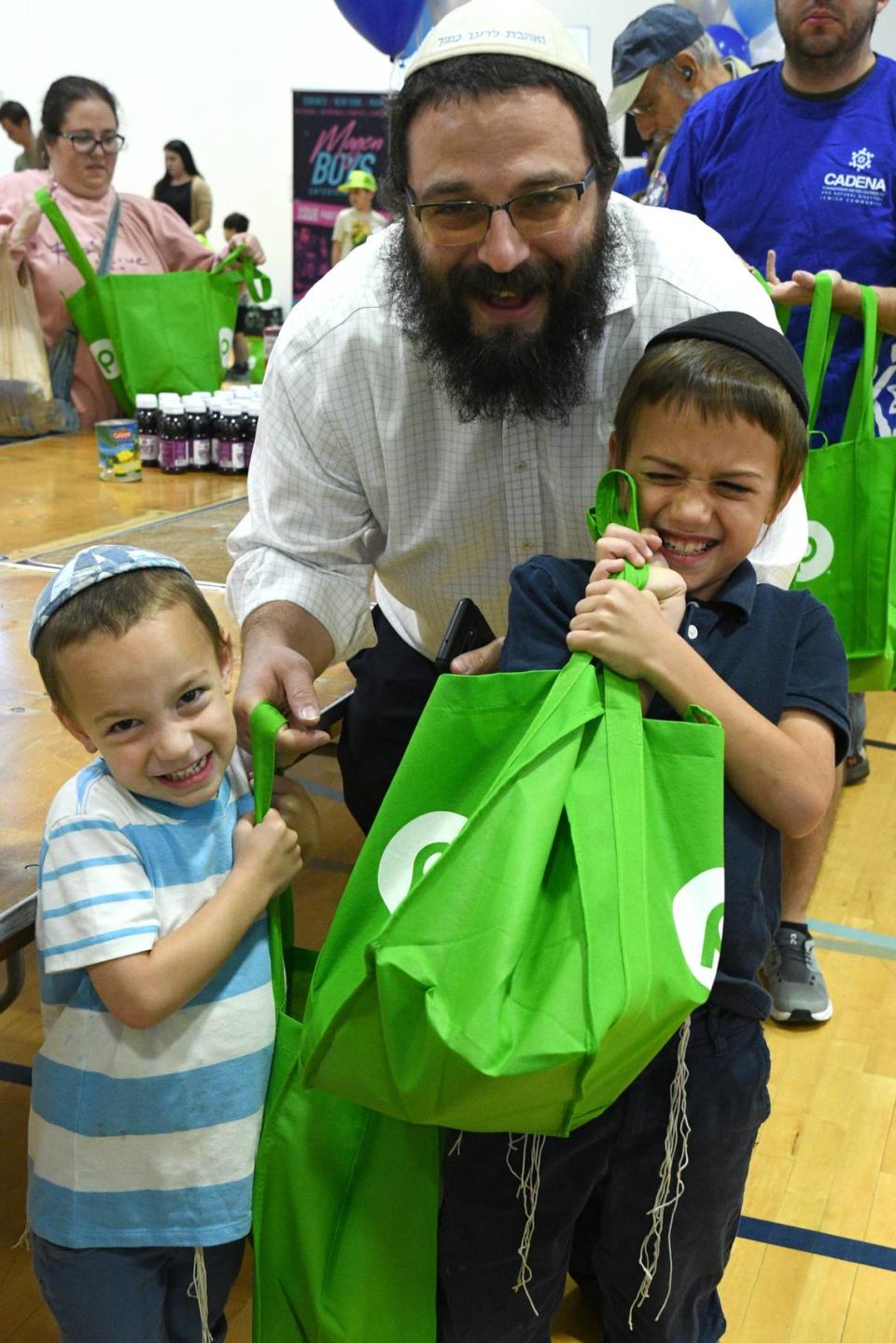 Una familia sostiene una bolsa de alimentos del Séder para ancianos y sobrevivientes del Holocausto en el evento anual Matzah Mitzvah de Jewish Community Services of South Florida.