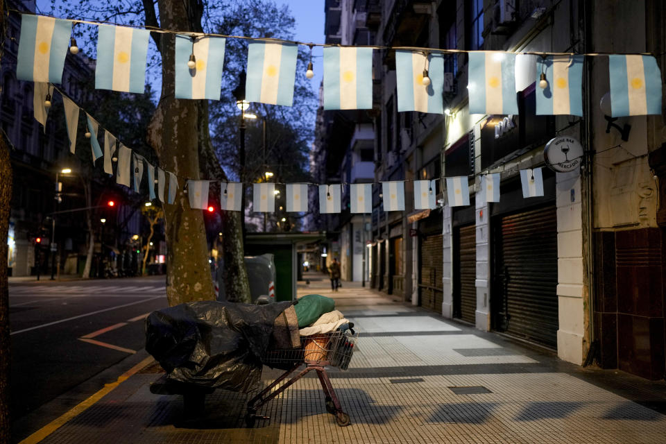 Una persona sin hogar duerme en una cama improvisada montada con un carro de la compra y un banco de la calle, en una zona decorada con banderas de Argentina, en Buenos Aires, Argentina, el miércoles temprano 27 de septiembre de 2023. (AP Foto/Natacha Pisarenko)