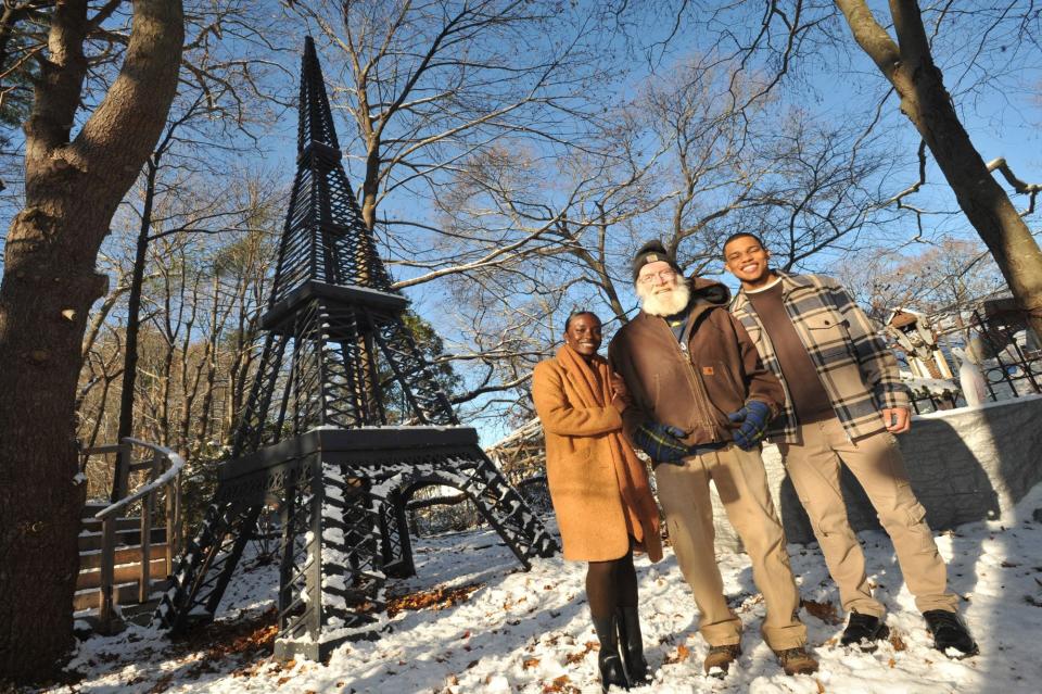 Amber Jogie, of Boston, left, and her fiance, Belmiro Da Veiga, of Brockton, right, pose with carpenter Steve Temple in his Abington backyard, where he built a model of the Eiffel Tower in front of which Belmiro proposed to Amber.