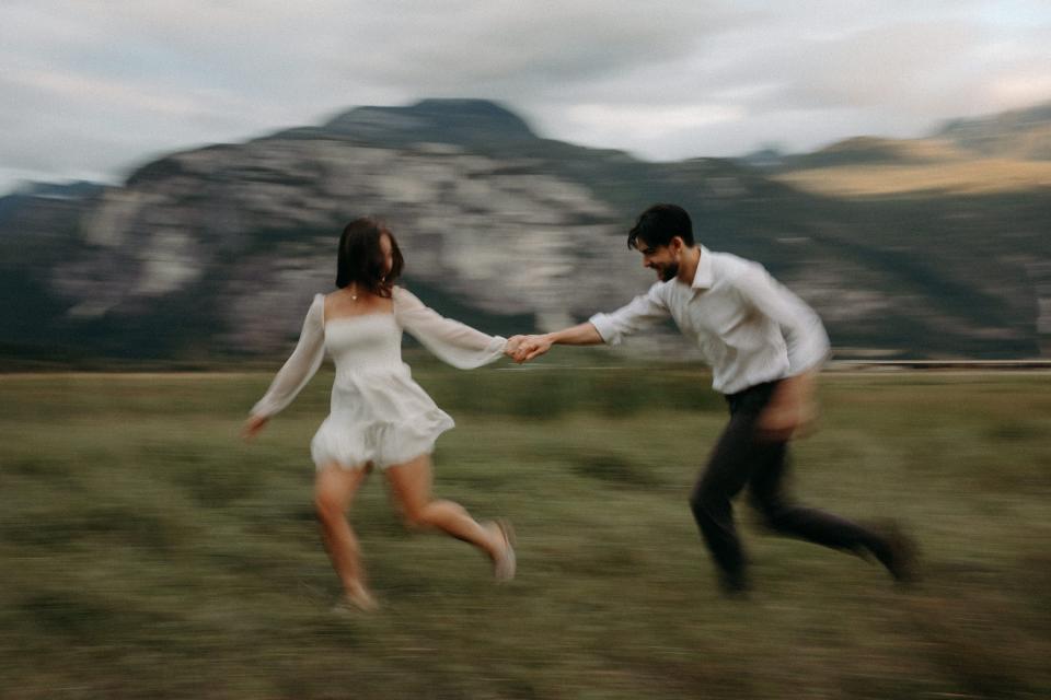 The couple is running through grass with a mountain in the background, with a slo-mo camera effect