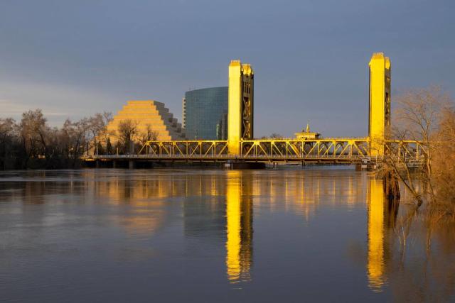 The Sacramento River, swollen from recent storms, flows under the Tower Bridge as the setting sun reflects off its golden paint on Monday, Jan. 9, 2023. A nearby gauge indicated the river was a 27.7 feet, still below monitor stage.