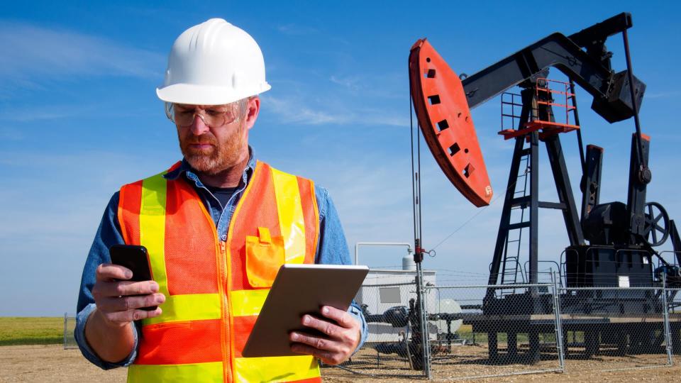 A royalty free image from the oil and gas industry of an engineer in front of a pumpjack drilling for natural gas and other resources.