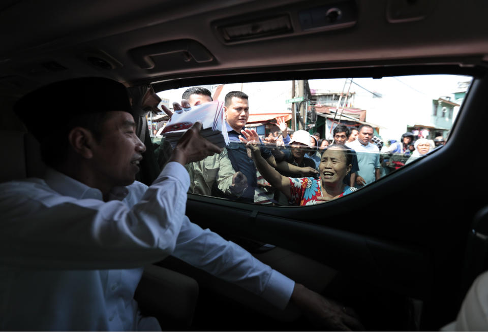 Indonesian President Joko Widodo hands out books to residents during his visit to Tanah Tinggi neighborhood in Jakarta, Indonesia, Friday, July 26, 2019. Indonesian President Joko Widodo said in an interview Friday that he will push ahead with sweeping and potentially unpopular economic reforms, including a more business-friendly labor law, in his final term because he is no longer constrained by politics. (AP Photo/Dita Alangkara)