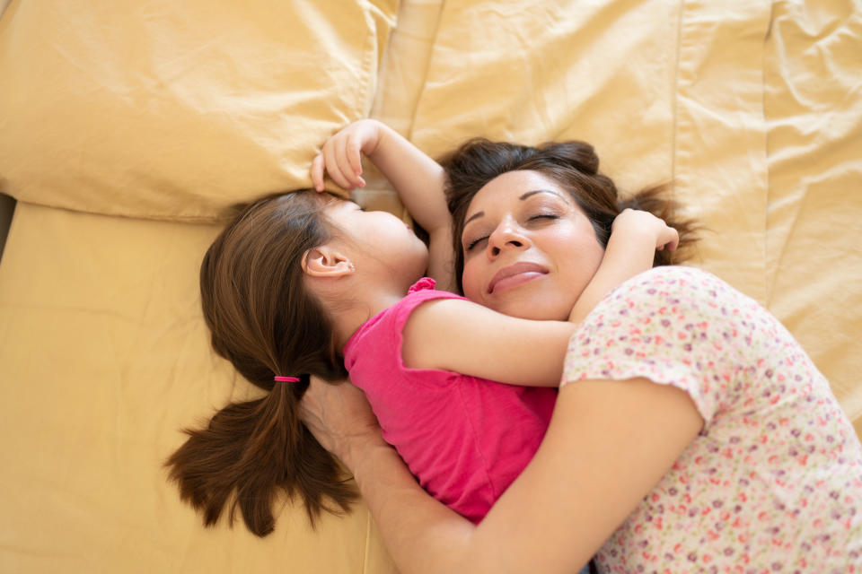 A mother and daughter hug as they co-sleep on the same bed at home