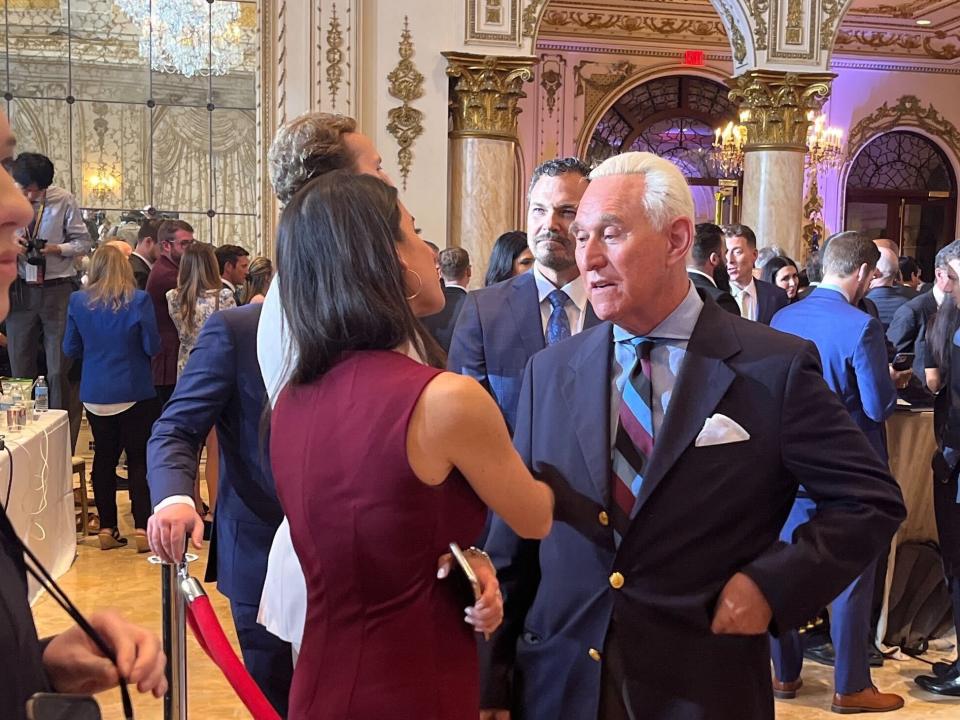 Roger Stone in a blue suit talking to a person in a red dress