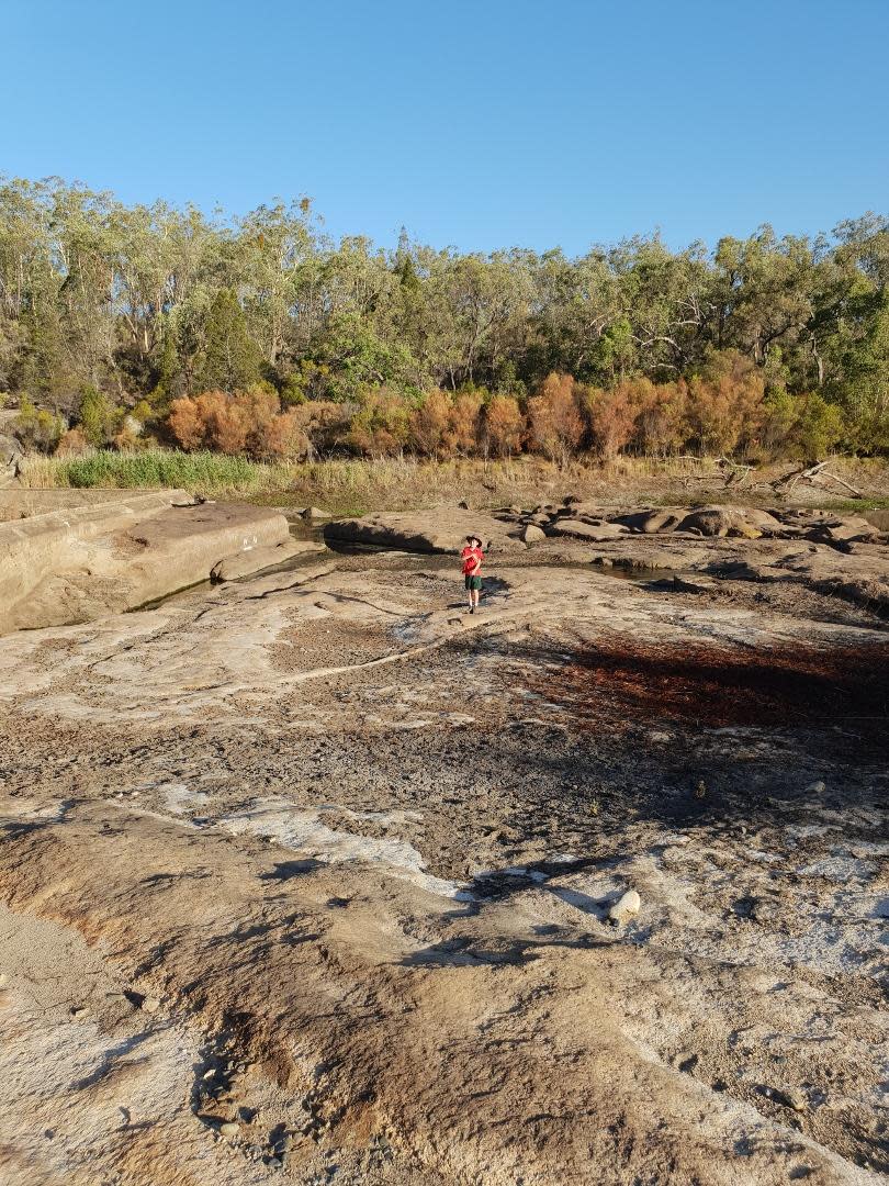 A young boy stands in a large dry river. 