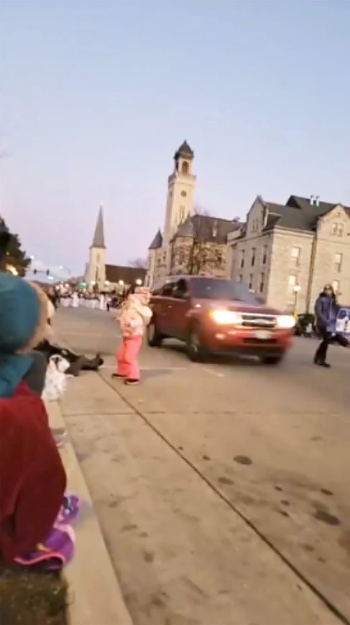 In this image taken from video an SUV speeds past a young girl and others attending a Christmas parade and continues to drive through the parade, injuring multiple people, Sunday, Nov. 21, 2021, in Waukesha, Wis.  (Jesus Ochoa via AP)