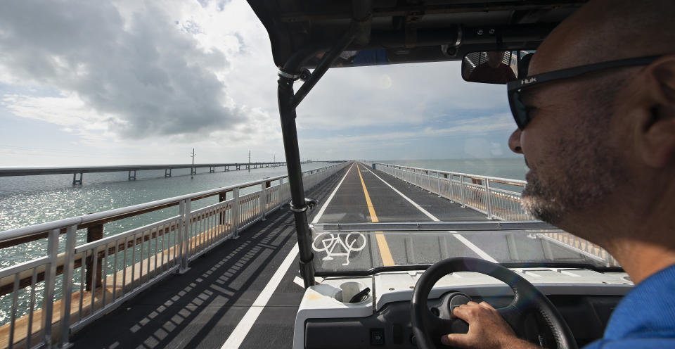 In this Monday, Jan. 10, 2022, photo provided by the Florida Keys News Bureau, Kelly McKinnon, executive director of the Pigeon Key Foundation, drives a cart on the Old Seven Mile Bridge. The historic bridge has undergone a 4.25-year, $44 million restoration effort and is to reopen Wednesday, Jan. 12, 2022, to pedestrians, bicyclists, anglers and visitors to Pigeon Key. The old bridge originally was part of Henry Flagler's Florida Keys Over-Sea Railroad that was completed in 1912. The railroad ceased operations in 1935 and was converted into a highway that opened in 1938. In 1982, construction was completed on a new Seven Mile Bridge, left, that continues to carry motor vehicles between the South Florida mainland throughout the Keys to Key West. (Andy Newman/Florida Keys News Bureau via AP)