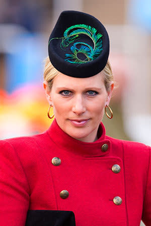 <p>Zara sets off her bold red coat with a hat topped with an iridescent peacock feather</p>