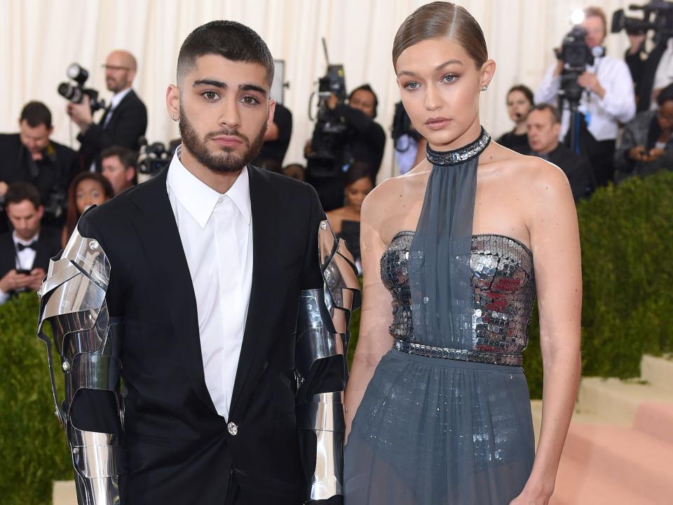 Zayn Malik at the 2016 Met Gala wearing a suit with metal armor on the arms with gigi hadid next to him in a blue gown