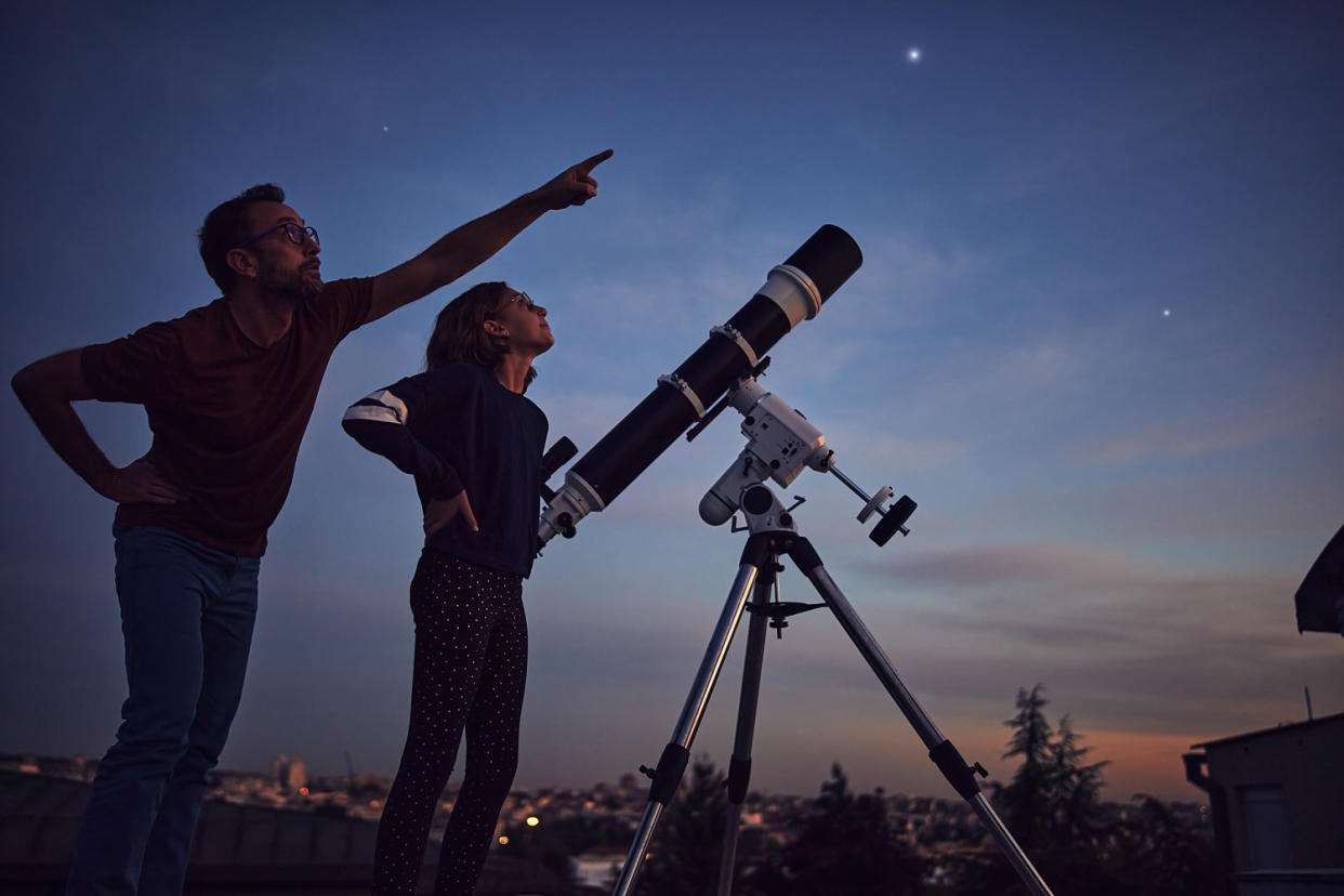 Silhouettes of father, daughter and astronomical telescope under starry skies. (m-gucci / Getty Images)