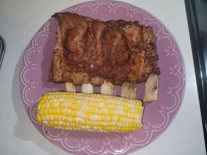Cooked ribs and corn on a plate.
