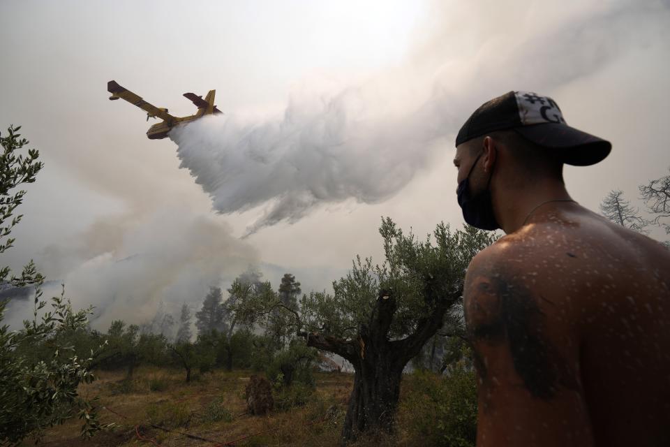 A local resident looks an aircraft dropping water over a wildfire at Ellinika village on Evia island, about 176 kilometers (110 miles) north of Athens, Greece, Monday, Aug. 9, 2021. Firefighters and residents battled a massive forest fire on Greece's second largest island for a seventh day Monday, fighting to save what they can from flames that have decimated vast tracts of pristine forest, destroyed homes and businesses and sent thousands fleeing. (AP Photo/Petros Karadjias)