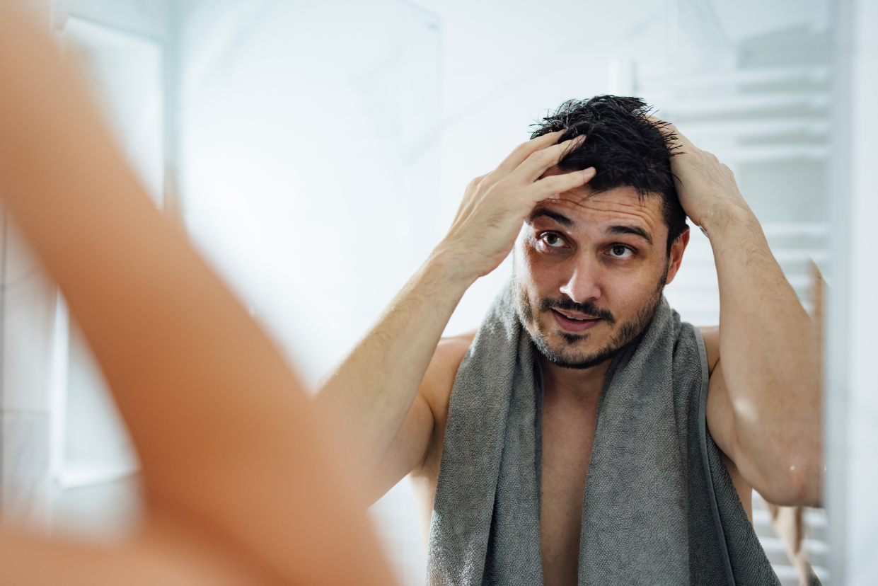 Man Inspecting His Hair While Looking in the Mirror After Showering With a Towel