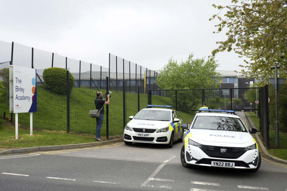 A photographer stands next to police cars at the entrance of the Birley Academy in Sheffield, northern England, on Wednesday, May 1, 2024. A 17-year-old boy was arrested on suspicion of attempted murder after three people were assaulted with a sharp object at a secondary school in northern England, South Yorkshire Police said Wednesday. Two adults suffered minor injuries and an injured child was being examined, police said. (Dominic Lipinski/PA via AP)
