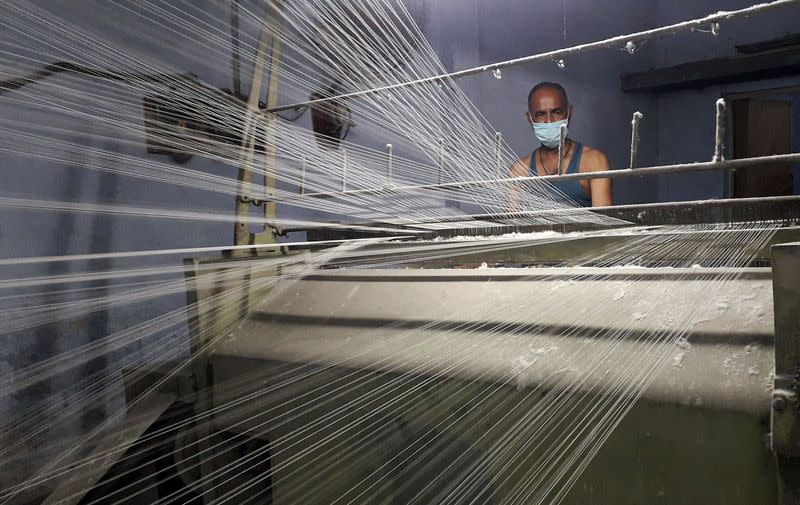 A worker wearing a protective face mask works on a loom in a textile factory in Meerut