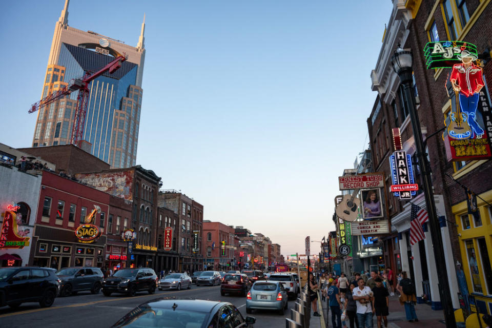 Busy street scene with neon signs, stores, and cars in a downtown district