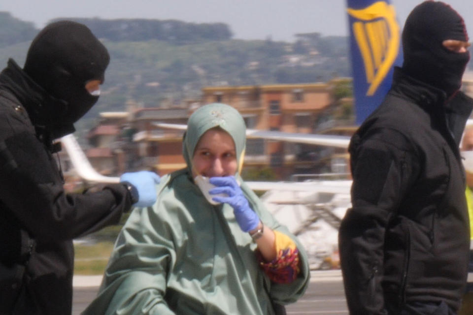 In this image taken from a video, Silvia Romano is flanked by two masked security officers as she walks on the tarmac after landing at Rome's Ciampino airport, Sunday, May 10, 2020. Wearing a surgical mask, disposable gloves and booties to guard against COVID-19, a young Italian woman has returned to her homeland after 18 months as a hostage in eastern Africa. (AP Photo/Paolo Santalucia)