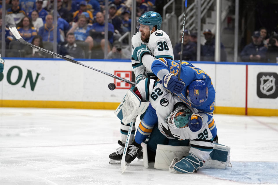 San Jose Sharks' Mario Ferraro (38) yells after getting hit in the chest with a puck as Sharks goaltender Mackenzie Blackwood (29) and St. Louis Blues' Jake Neighbours (63) collide during the second period of an NHL hockey game Saturday, March 30, 2024, in St. Louis. (AP Photo/Jeff Roberson)