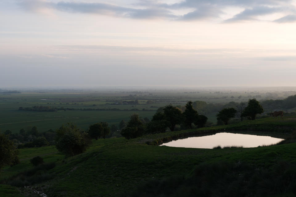 Sunset over some green fields with a small lake in the foreground