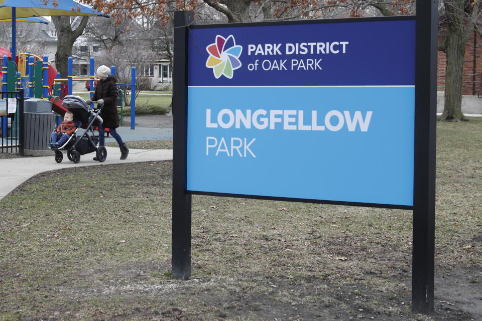 A resident of the Village of Oak Park, Ill., walks with a child in Longfellow Park, Friday, March 20, 2020. There are at least three confirmed cases of COVID-19 in Oak Park, just nine miles from downtown Chicago, where the mayor has ordered residents to shelter in place. With so few tests available, surely there are others, says Tom Powers, spokesman for the village of about 52,000 in a metropolitan area with millions. (AP Photo/Charles Rex Arbogast)