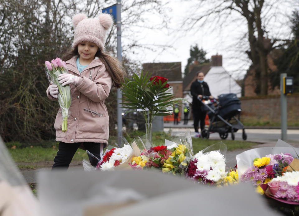 A young girl lays a floral tribute to Captain Tom Moore in Marston Moretaine, England, Wednesday, Feb. 3, 2021. Captain Tom Moore, the 100-year-old World War II veteran who captivated the British public in the early days of the coronavirus pandemic with his fundraising efforts for medical care workers, died Tuesday. (AP Photo/Alastair Grant)