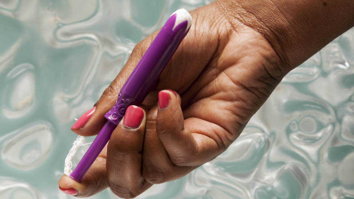 An unwrapped tampon in a woman’s hand.