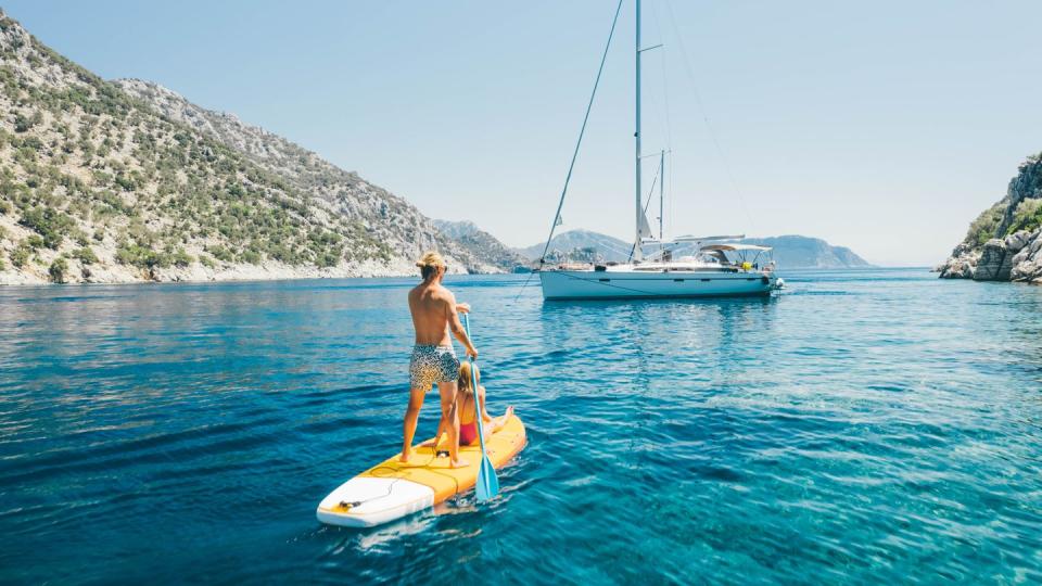 young couple paddling on stand up paddleboards against the yacht in the sea