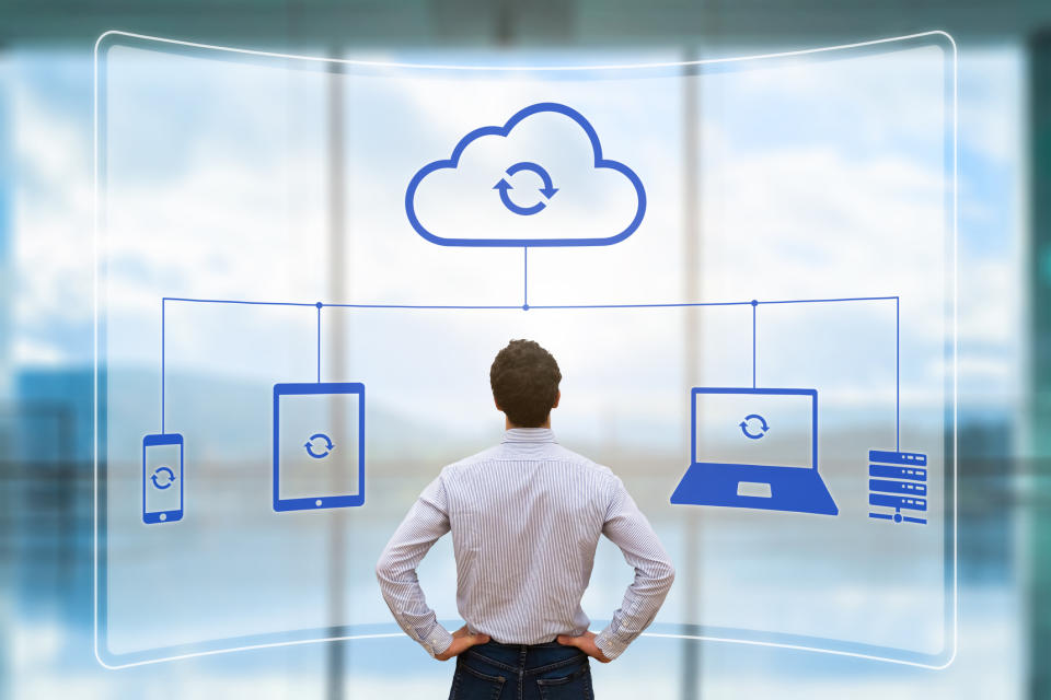 A man looking at a visualization of several electronic devises syncing in the cloud.