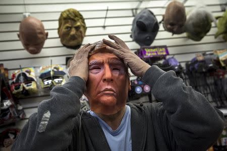 Employee Kenny Lomi adjusts a Halloween mask of Republican presidential candidate Donald Trump as he poses for a photo at the Village Party Store halloween headquarters in the Manhattan borough of New York, October 15, 2015. REUTERS/Andrew Kelly