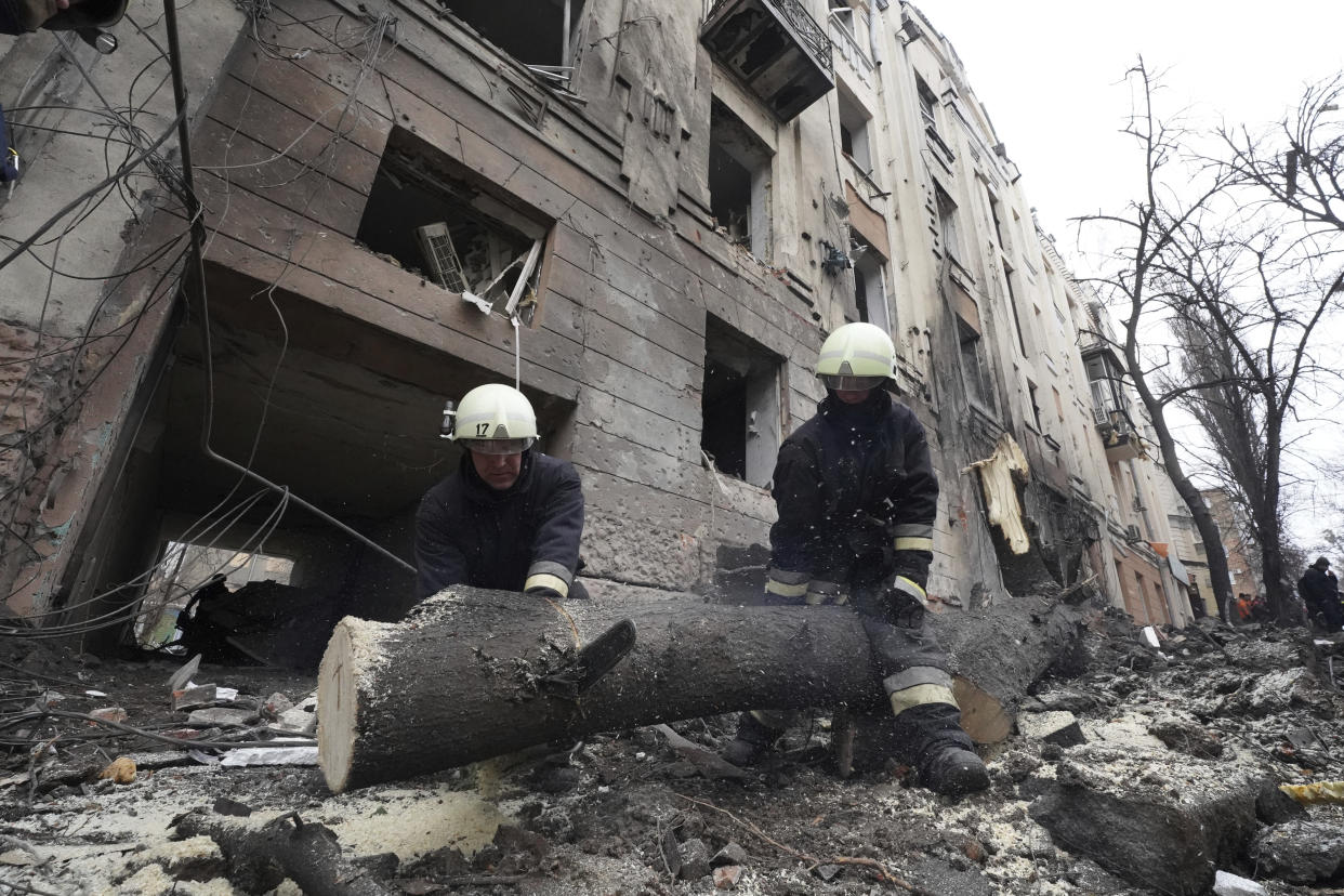 Emergency workers saw a tree in front of a residential building which was hit by a Russian rocket at the city center of Kharkiv, Ukraine, Sunday, Feb. 5, 2023. (AP Photo/Andrii Marienko)