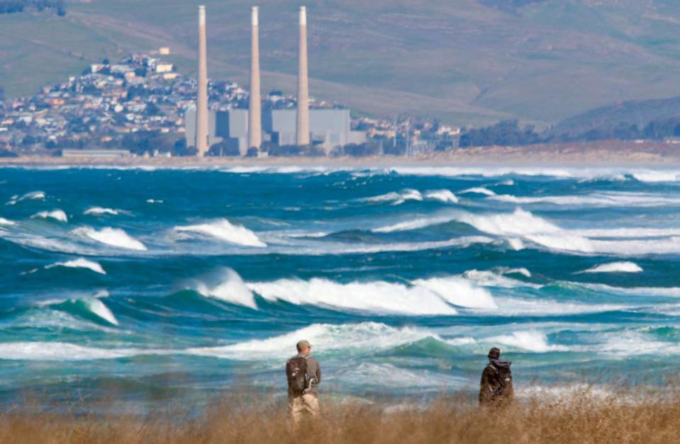 From the bluff trail south of Spooner’s Cove, hikers at Montana de Oro State Park watch the high surf in February 2020 with the mothballed Morro Bay Power Plant in the background.