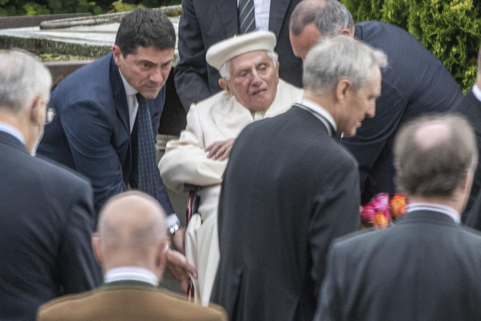 El papa emérito Benedicto XVI es auxiliado en su silla de ruedas durante la visita a la tumba de sus padres y hermana en el cementerio Ziegetsdorf, cerca de Ratisbona, Alemania, el sábado 20 de junio de 2020. (Armin Weigel/dpa vía AP)