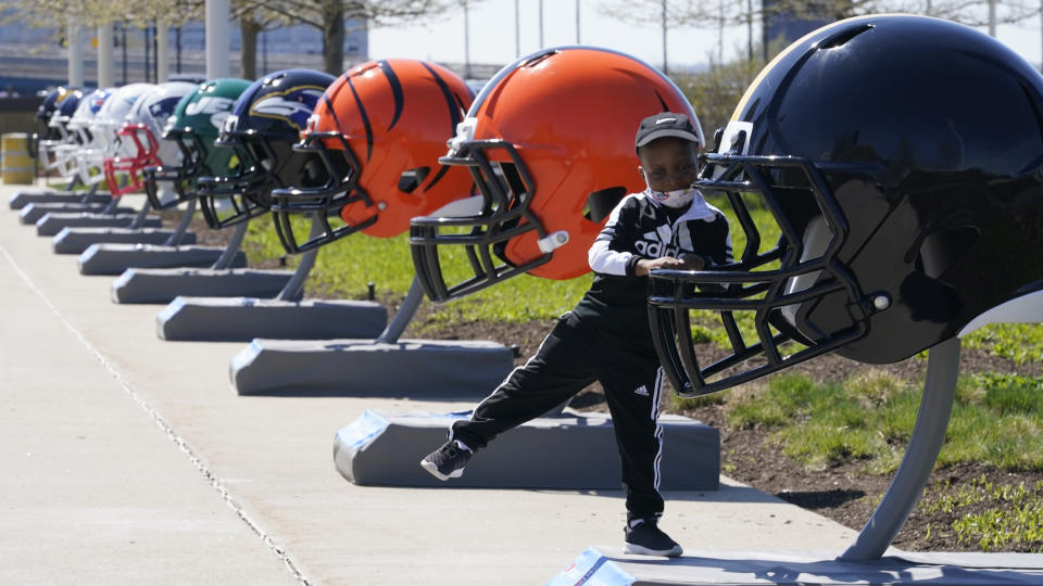 Joseph Toliver, 4, plays on one of the 32 NFL team helmets on display, Tuesday, April 13, 2021, in downtown Cleveland. Forced to cancel last year's NFL Draft in Las Vegas, the league is using lessons learned while plowing through an unprecedented, socially-distanced 2020 season and holding the Super Bow in Tampa, to have a draft that will look much more like normal — well, the new normal — with fans wearing their favorite team's colors and required masks.(AP Photo/Tony Dejak)